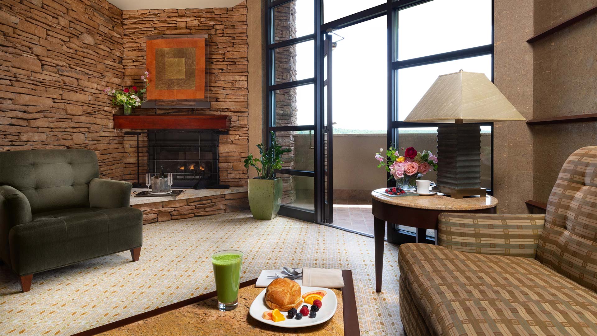 interior shot of Falling Rock's king suite living area. There is a couch and an arm chair around a coffee table with breakfast on it. There is a fireplace in the background and a door leading out onto a balcony