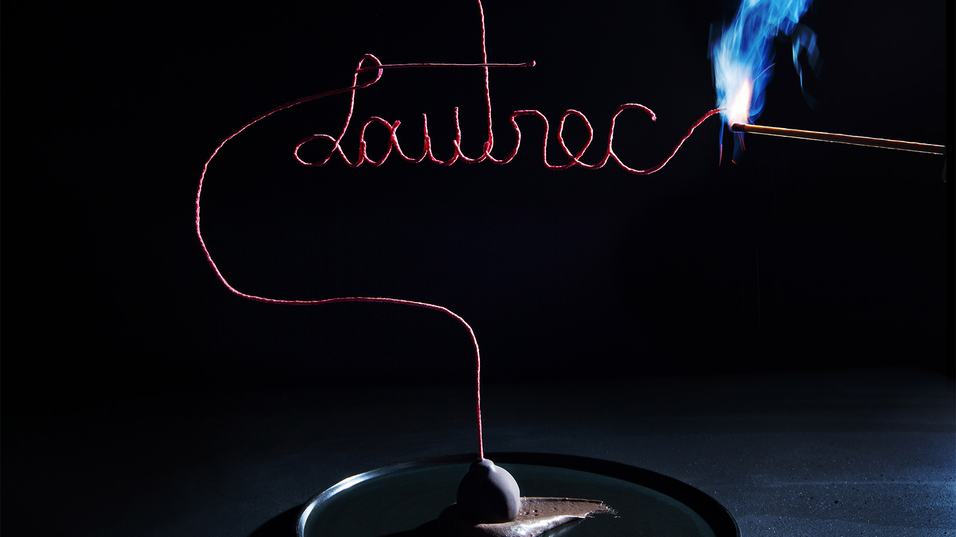 fancy wick spelling "Lautrec" in cursive being lit with a match