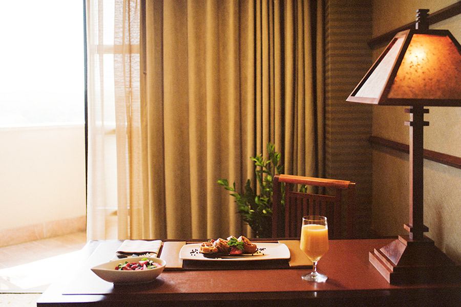 Waffles, orange juice, and a bowl of fruit is placed on a brown wooden table in a well light room.
