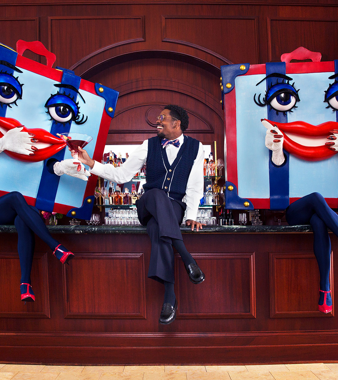 a man sitting on a bar in between two costumed women dressed with boxes as heads