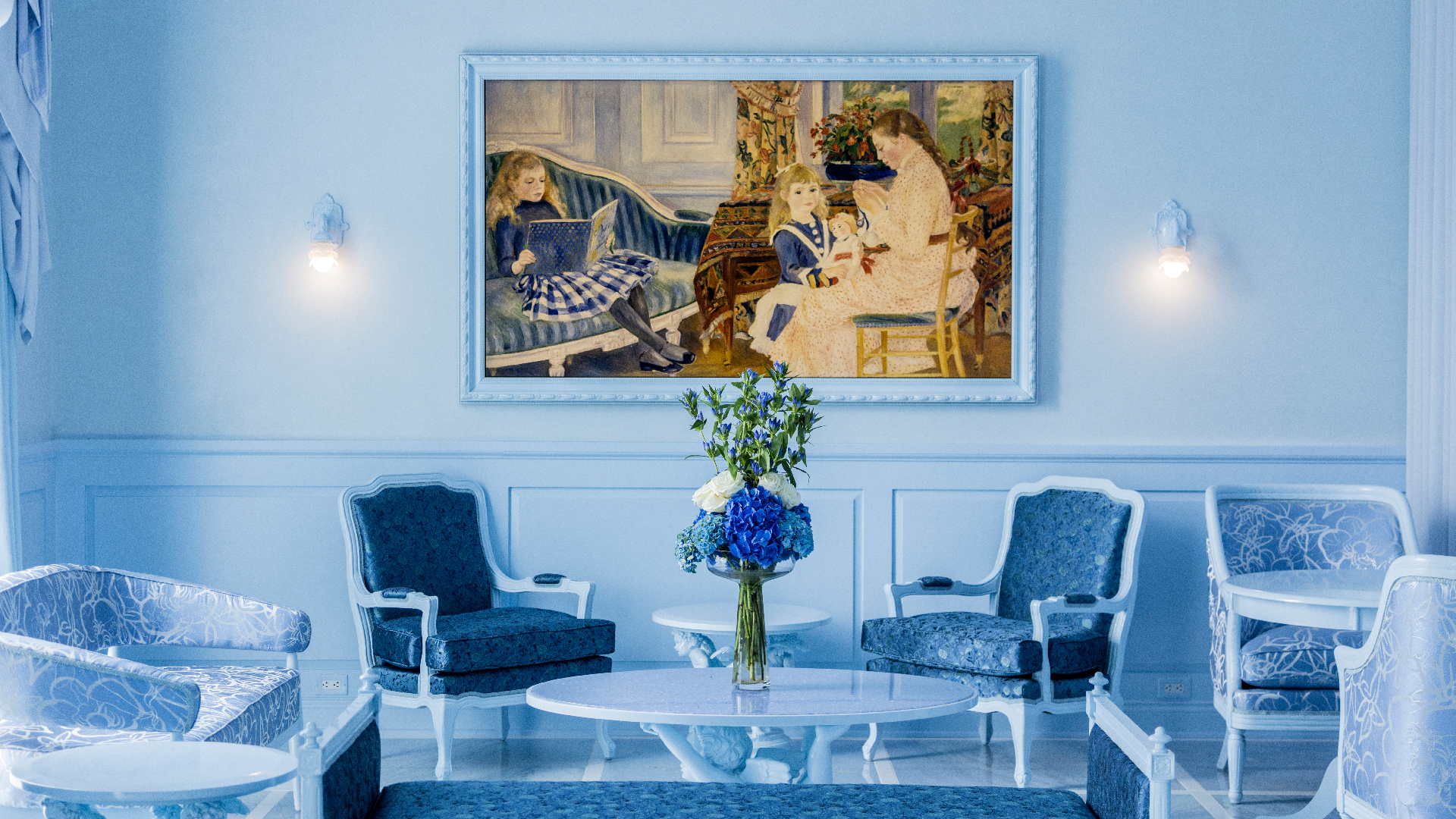 a beautiful painting projected by a television above two blue chairs in front of a blue table with a vase of blue flowers