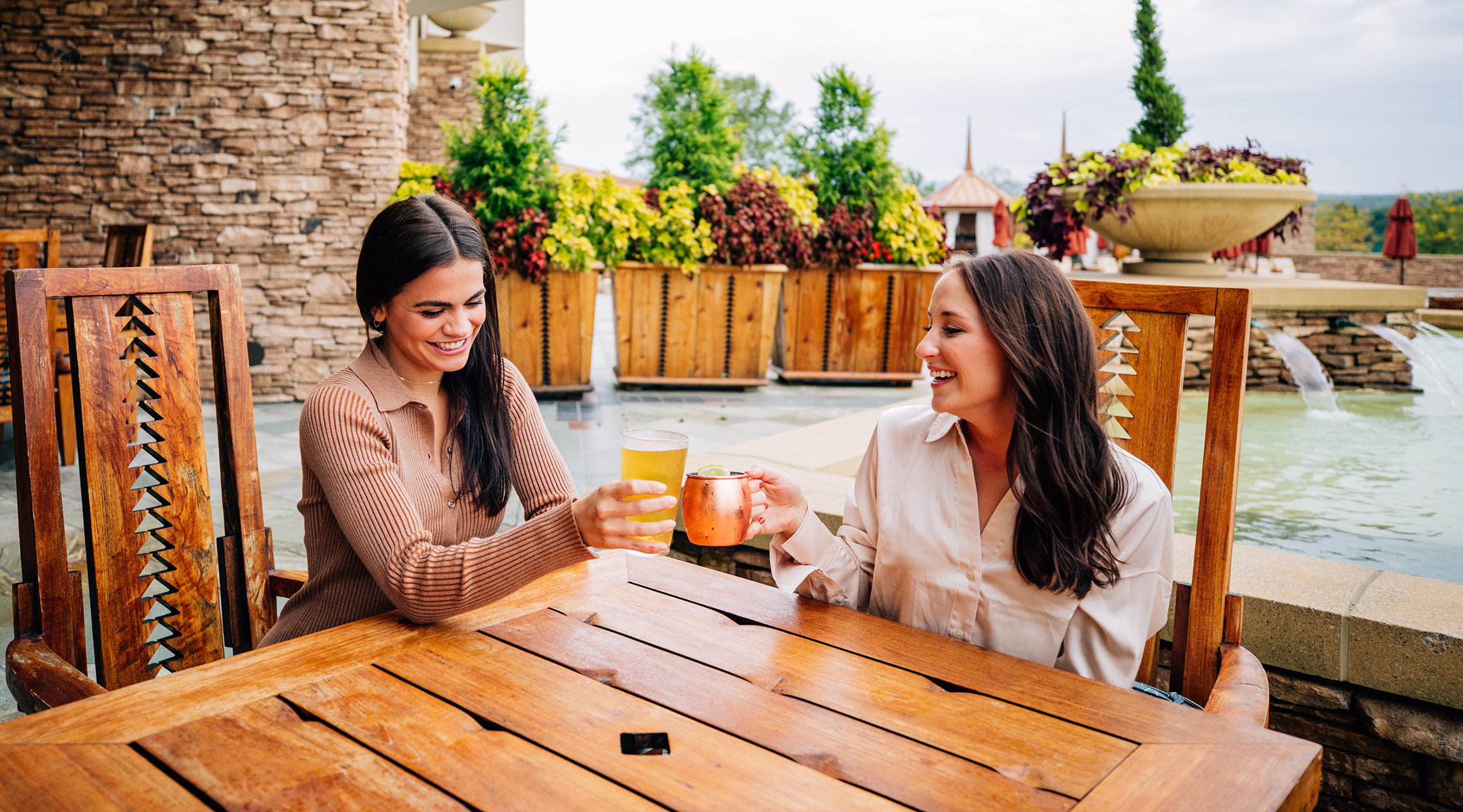 Two women toasting with drinks on a patio at Falling Rock at Nemacolin