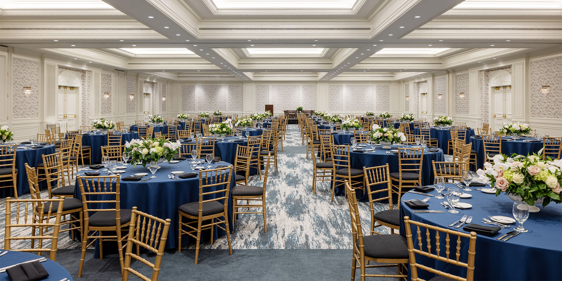 Ballroom with round tables dressed in blue tablecloths and wooden chairs