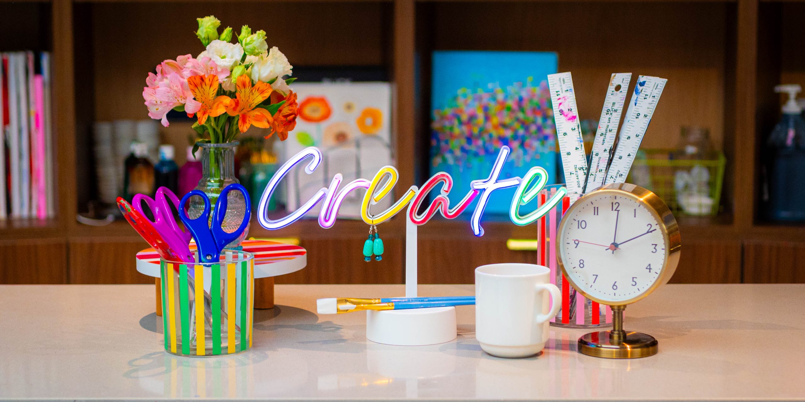 Items on a table include a colorful sign with the word "Create," a coffee mug, a clock, scissors, flowers, and rulers.