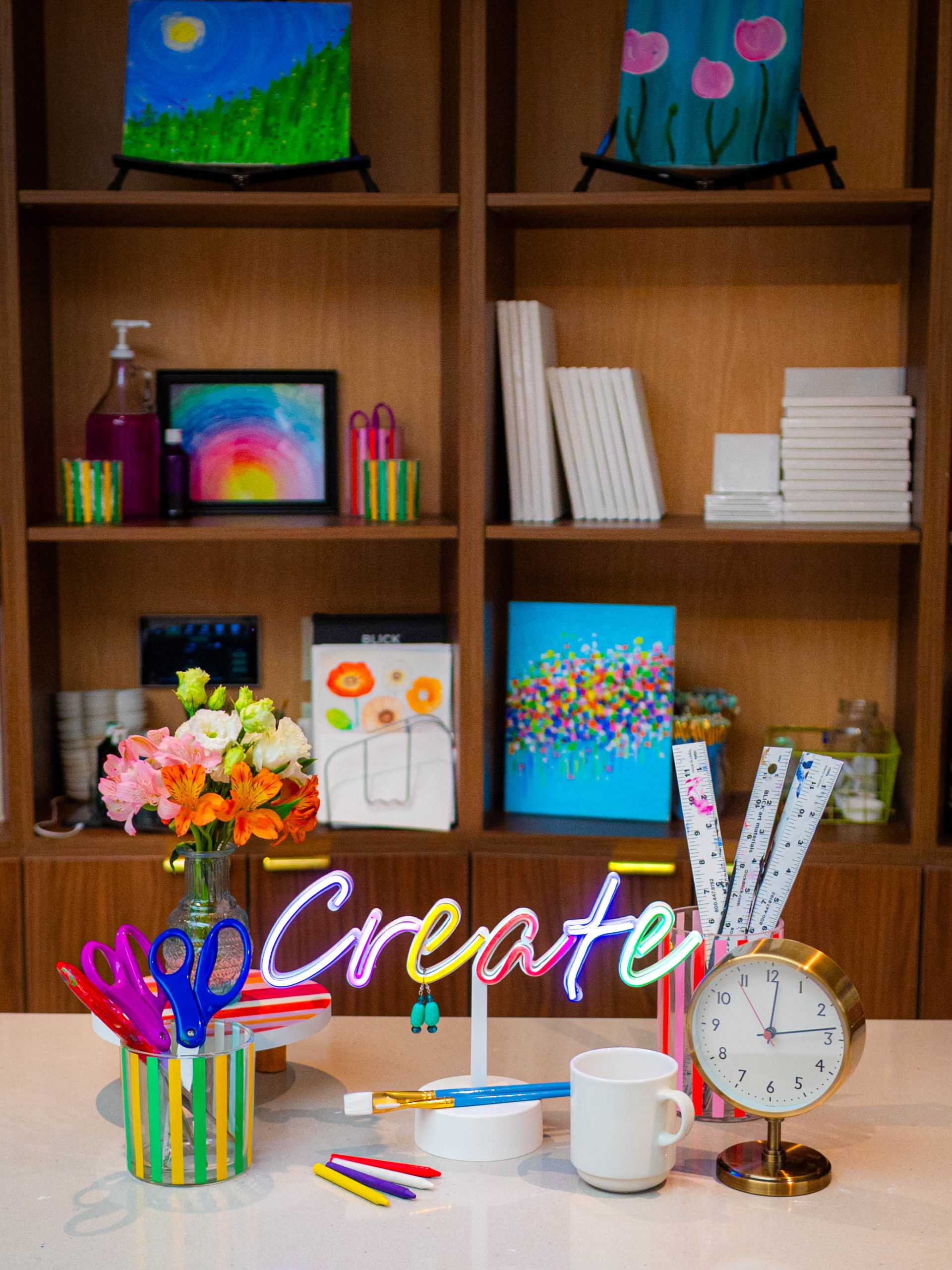 Items on a table include a colorful sign with the word "Create," a coffee mug, a clock, scissors, flowers, and rulers.