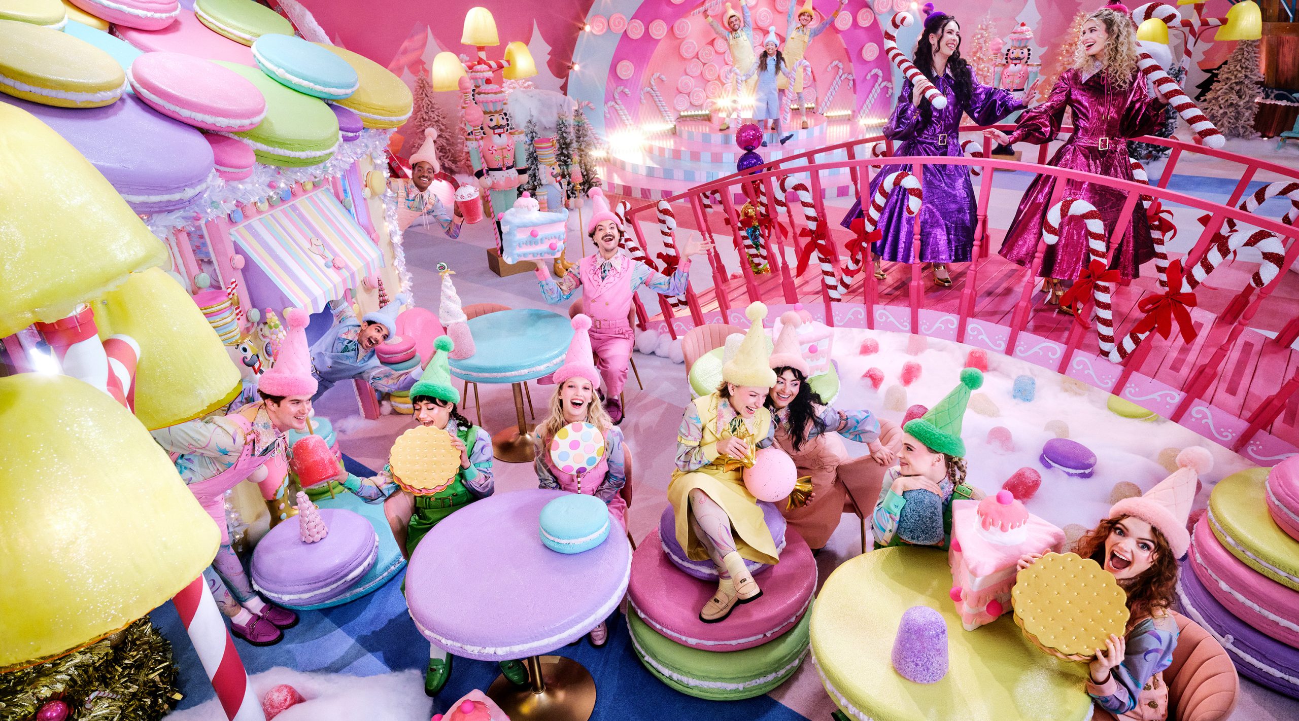 Male and female elves dressed in pastel-colored outfits interact with one another an giant macarons and candy canes in a larger-than-life scene at Hardy's Holiday Village at Nemacolin