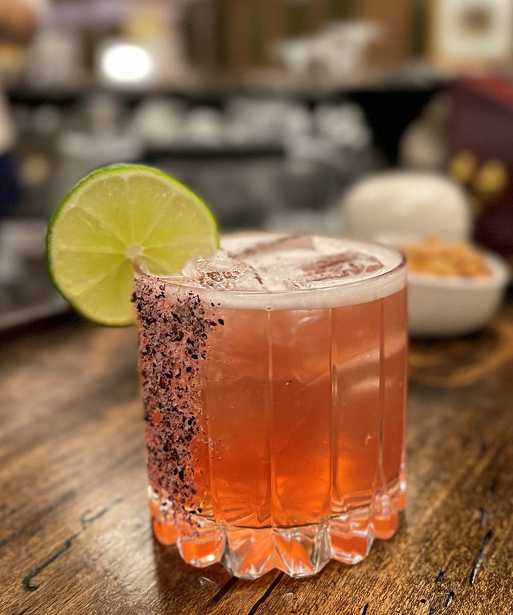 orange drink in a rocks glass garnished with a lemon and hibiscus salt