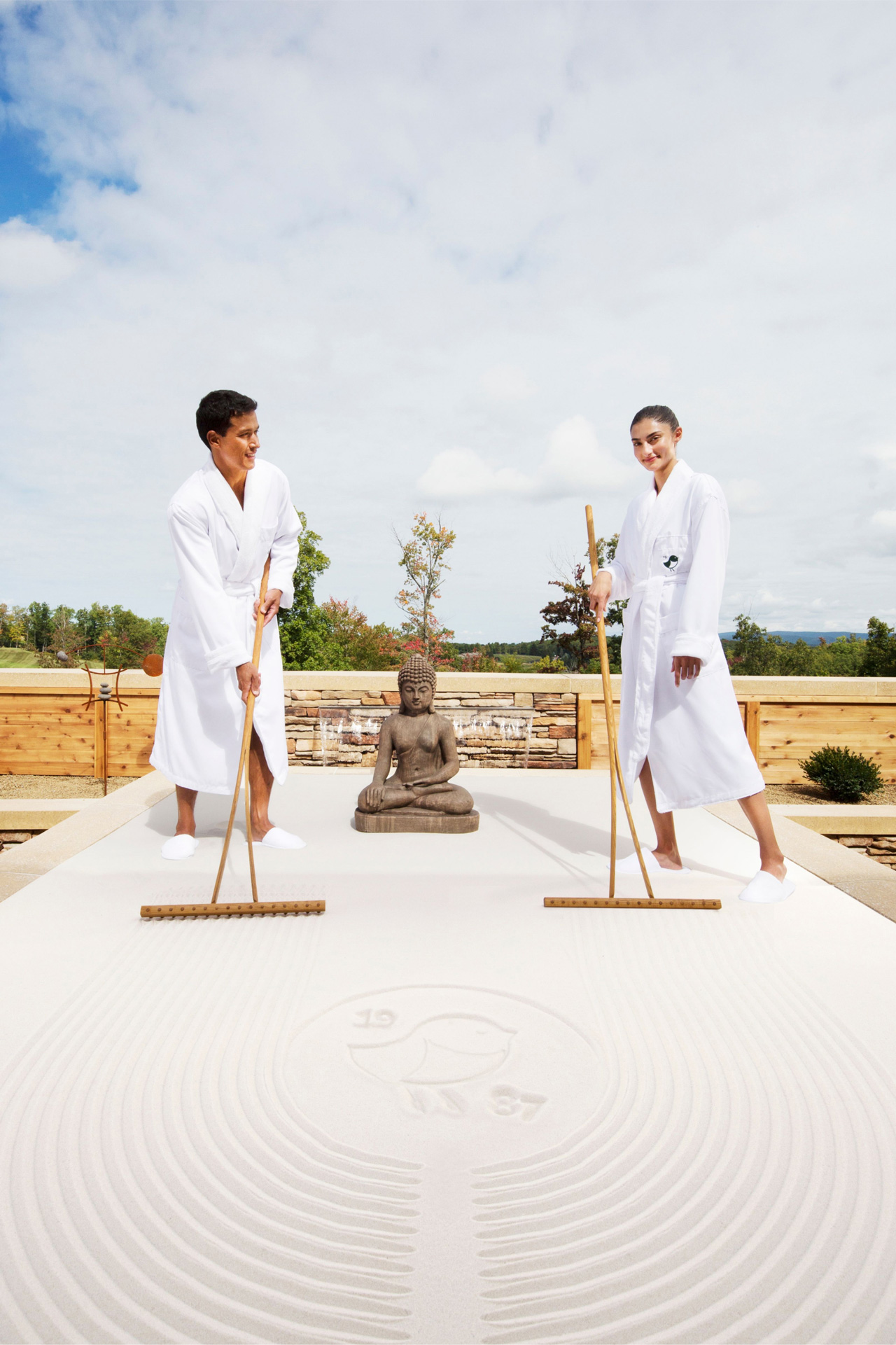 Click here to open the gallery overlay for the image: two people in bathrobes with a Buddha engaging in life size sand tray therapy