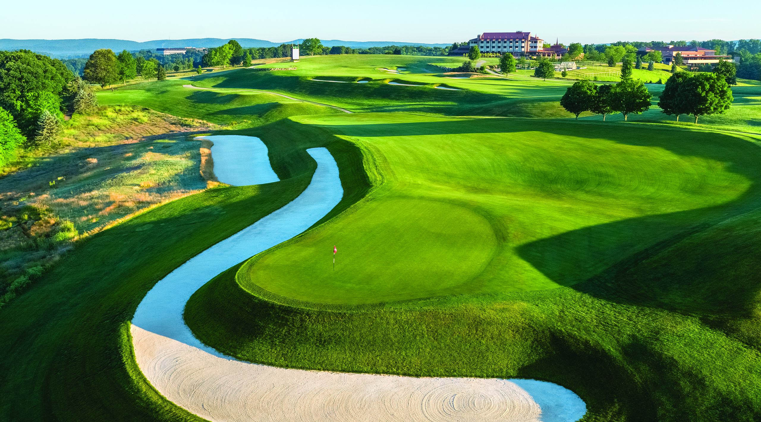 Aerial drone photo of the #1 hole on Mystic Rock Golf Course at Nemacolin resort, with the 18th hole and the Falling Rock hotel in the background