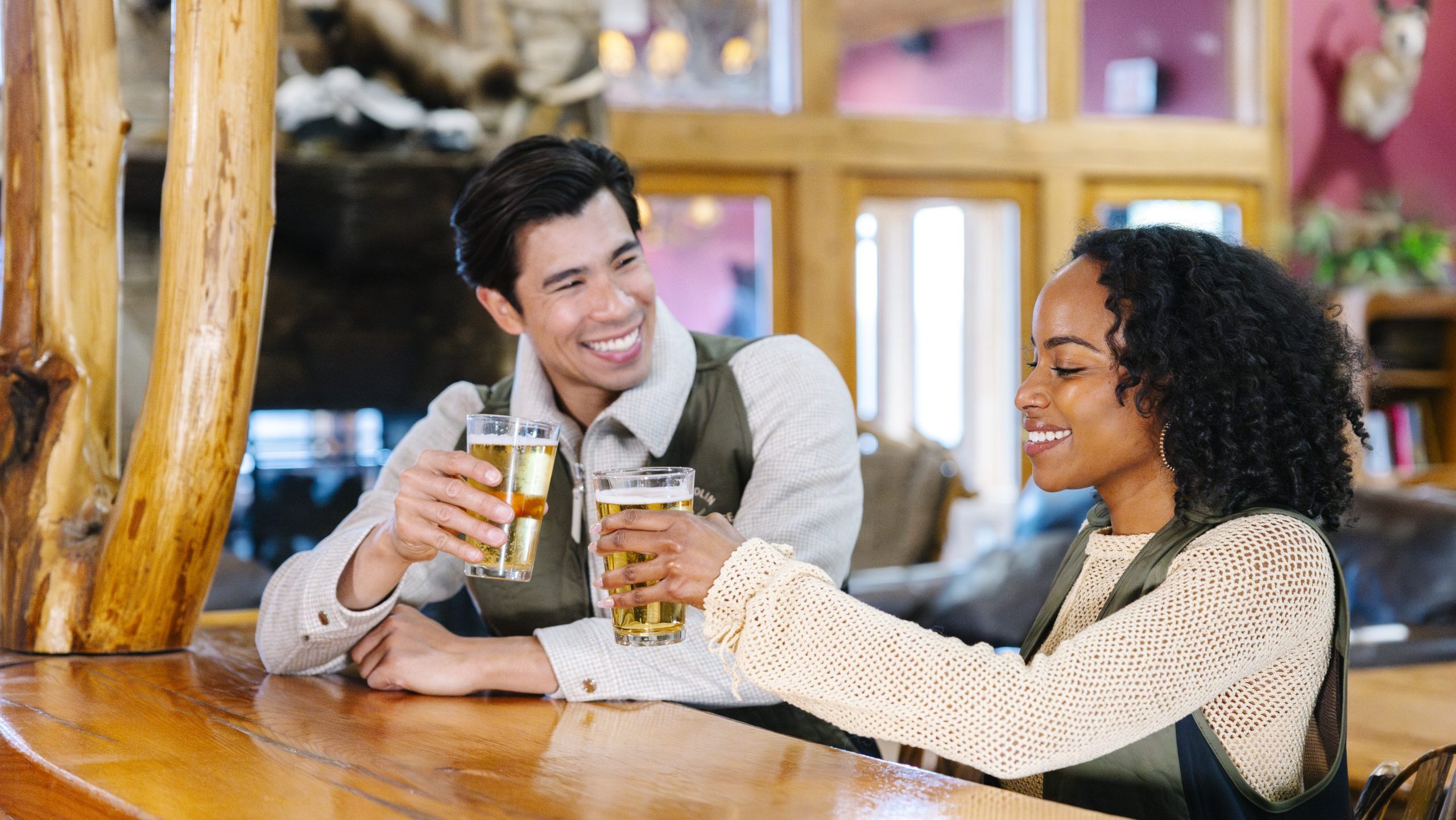 A man, left, and a woman, right, each hold up a pint of beer as they toast together inside Orville's Pub and Grill.