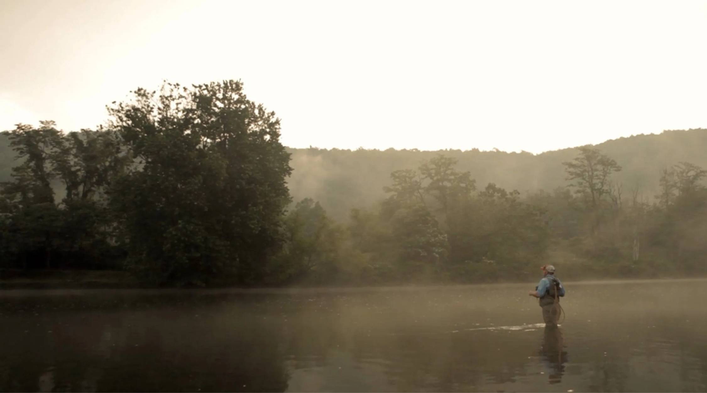 A man stands in a river, fly fishing on a foggy morning.