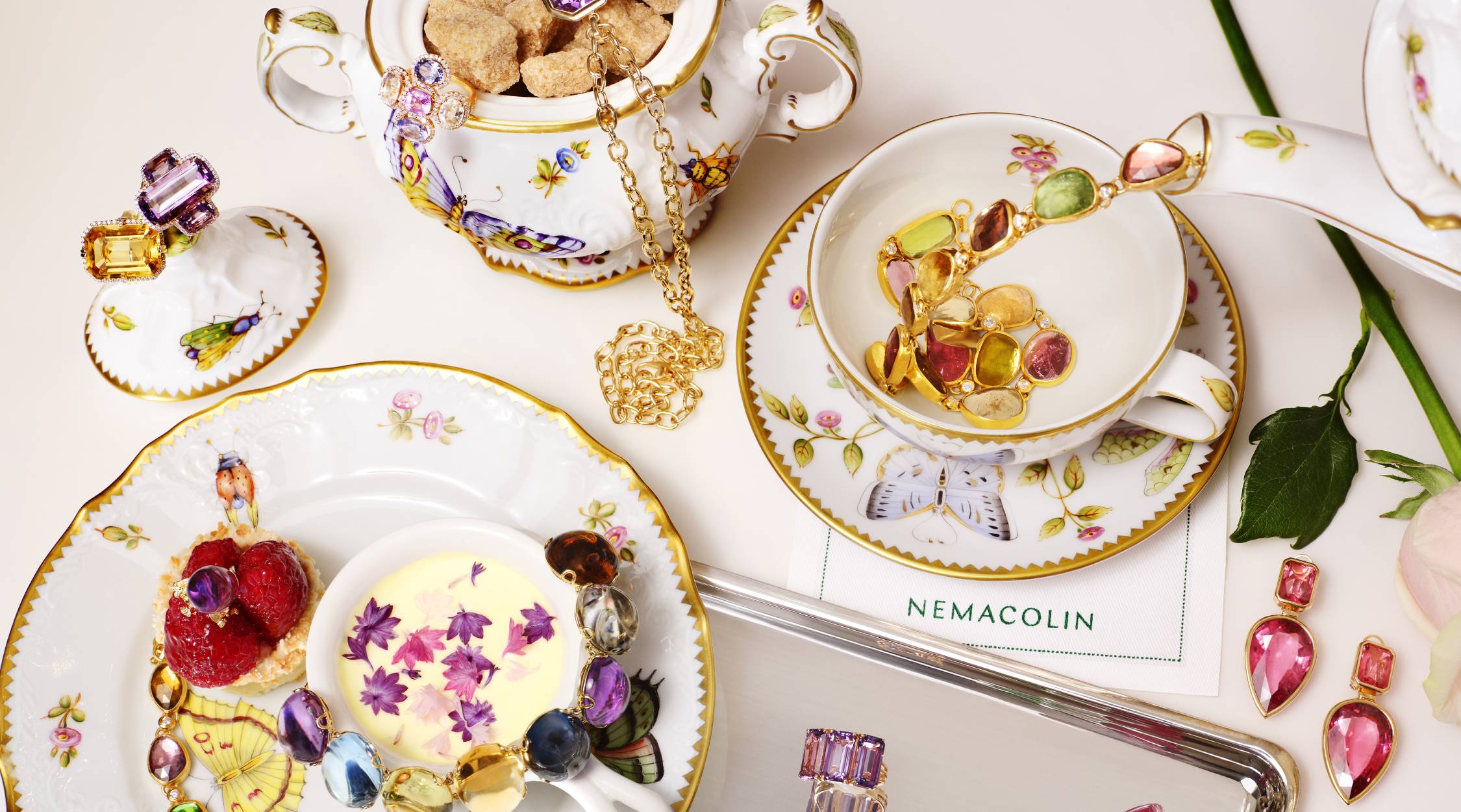 Tea cups are set, but rather than tea pouring from the pot, a necklace of jewels spills into the cup. A white napkin has the word Nemacolin printed on it.